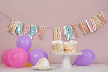 Doğum günü süslemeleri ve pembe duvarın yanındaki masada lezzetli pastalarla dikilmek.