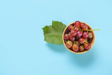 Lezzetli olgun üzümlü kase ve mavi arka planda yaprak