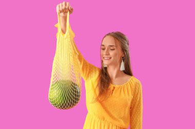 Mor arka planda sicim torbasında taze karpuz olan genç bir kadın.