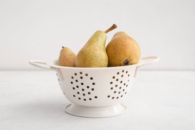 Beyaz zemin üzerinde olgun armutları olan Colander