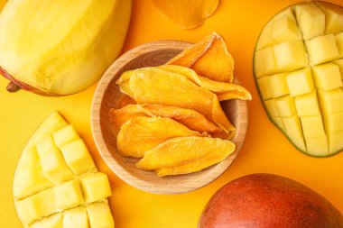 Turuncu arka planda kurutulmuş mango dilimleri olan ahşap kase.