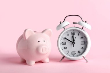 Pembe arka planda çalar saati olan domuz kumbarası