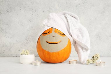 Kil maskeli balkabağı, çiçekler, krema ve mumlar beyaz masada.