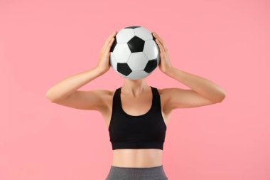Pembe arka planda futbol topu olan genç ve güzel bir bayan.