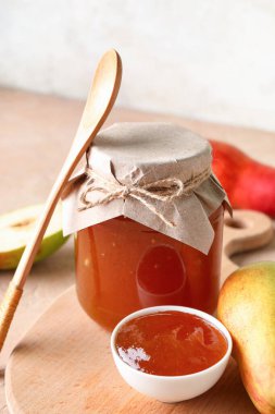 Cam kavanoz ve bir kase armut reçeli. Masada tahta tahta var.