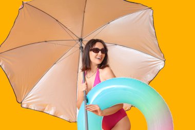 Sarı arka planda şişirilebilir yüzüğü ve şemsiyesi olan güzel genç bir kadın.