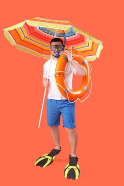 Yüzgeçli yakışıklı genç adam, şnorkelli maske, kırmızı arka planda can simidi ve şemsiye.