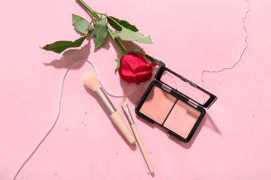Kırmızılı kompozisyon, makyaj fırçaları ve pembe arkaplanda suda güzel kırmızı gül çiçeği.