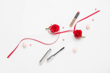 Şık ruj, rimel, kurdele ve beyaz arka planda güzel kırmızı gül çiçekleri olan kompozisyon.