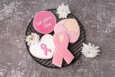 Pembe kurdeleli kurabiyeler ve gri grunge arka planda destekleyici kelimeler. Göğüs kanseri farkındalığı konsepti