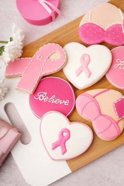 Pembe kurdeleli kurabiyeler ve gri grunge arka planda destekleyici kelimeler. Göğüs kanseri farkındalığı konsepti