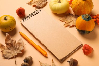 Renkli arka planda boş defter, kalem, balkabağı ve doğal orman dekoru içeren kompozisyon, yakın plan