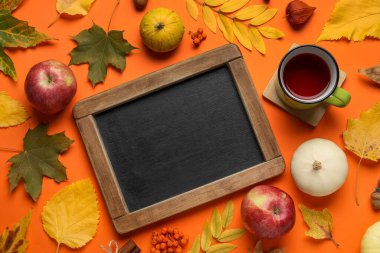 Renk arkaplanında boş karatahta, bir fincan çay ve sonbahar yapraklı kompozisyon