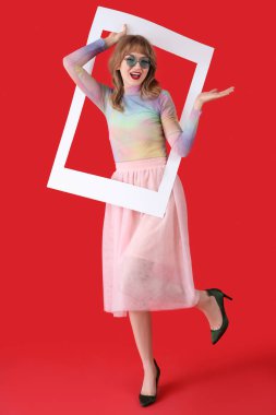 Kırmızı arka planda çerçeveli güneş gözlüklü genç bir kadın.