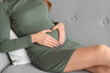 Genç hamile kadın evdeki kanepede uzanıyor, yakın plan.