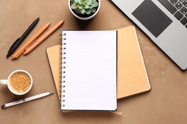 Notebook with laptop and cup of tasty coffee on brown background