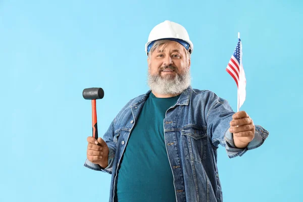 Portrait of senior man in hardhat with rubber mallet and USA flag on blue background. Labor Day celebration