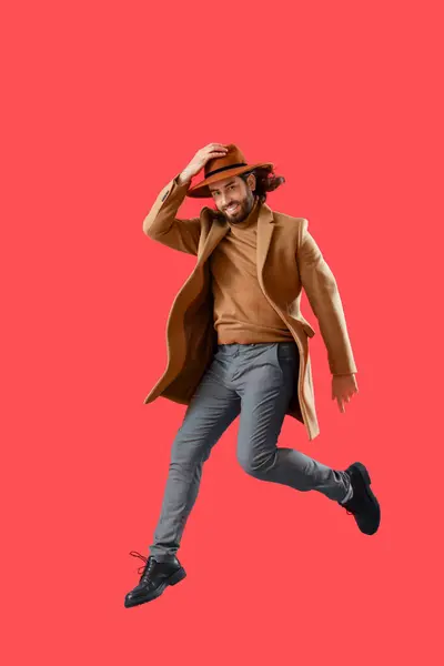 Jumping Young Man Coat Hat Red Background — Stock Photo, Image