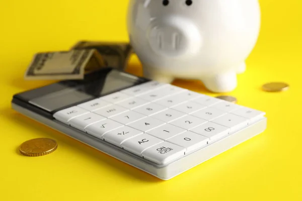 Piggy bank, calculator and money on yellow background