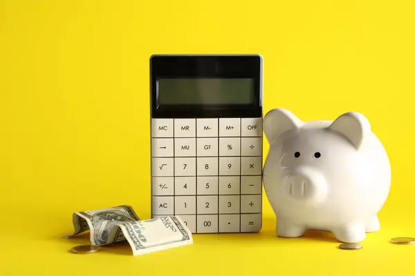 Piggy bank, calculator and money on yellow background