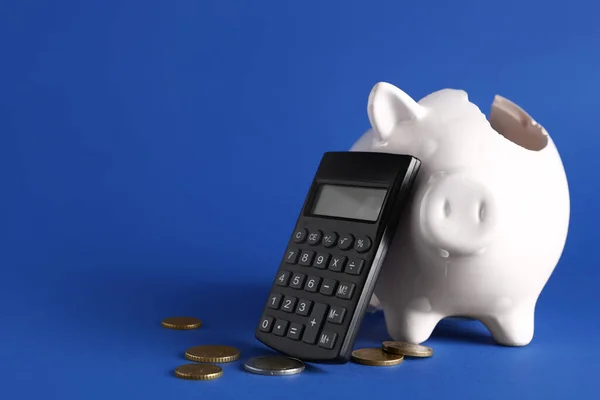 Broken piggy bank with coins and calculator on blue background