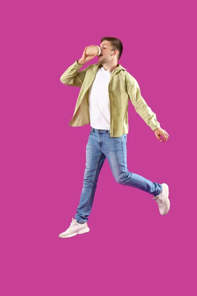 Прыгающий Молодой Человек Пьет Кофе Пурпурном Фоне — стоковое фото