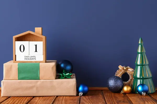 Countdown calendar with Christmas decorations and gift boxes on brown wooden table near blue wall