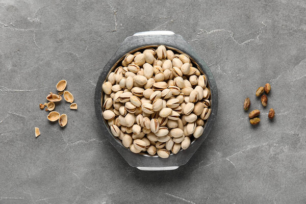 Metal bowl with tasty pistachio nuts on grey background