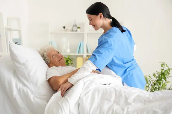Γυναίκα Νοσοκόμα Βάζοντας Ηλικιωμένη Γυναίκα Στο Κρεβάτι Στην Κρεβατοκάμαρα — Φωτογραφία Αρχείου