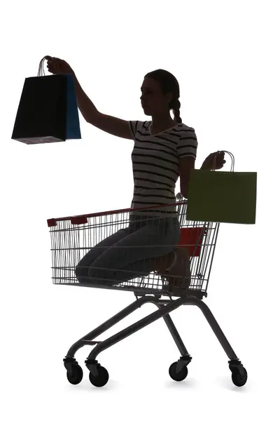 白い背景にショッピングカートに座っているバッグを持つ若い女性のシルエット — ストック写真