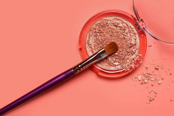 Makeup brush and broken highlighter on red background