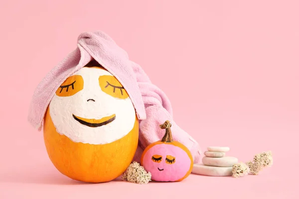 Pumpkins with masks, flowers and spa stones on pink background