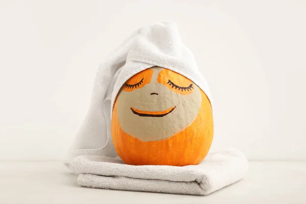 Pumpkin with clay mask and towels on light background