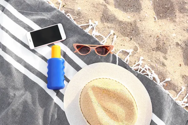 Stylish sunglasses with phone and beach accessories on sandy background