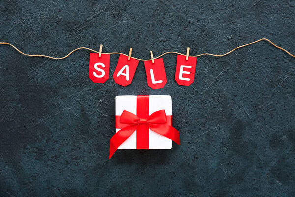 Подарочная коробка, веревка, прищепки и флаги со словом ПРОДАЖА на черном фоне