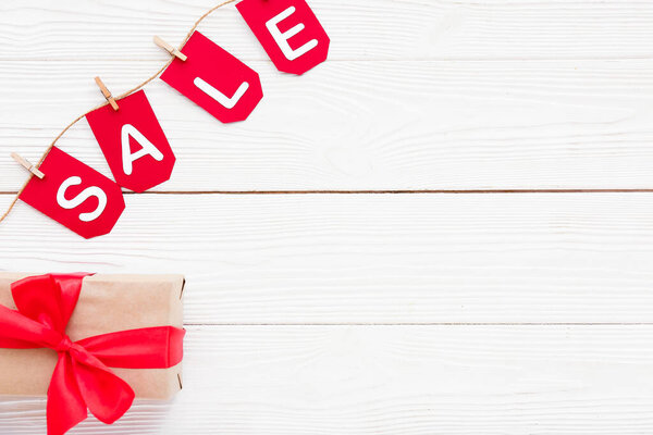 Подарочная коробка, веревка, прищепки и флаги со словом ПРОДАЖА на белом деревянном фоне
