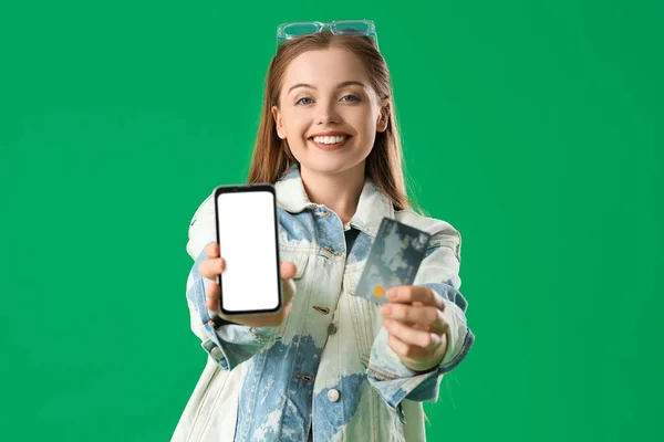 Young woman with credit card and mobile phone on green background