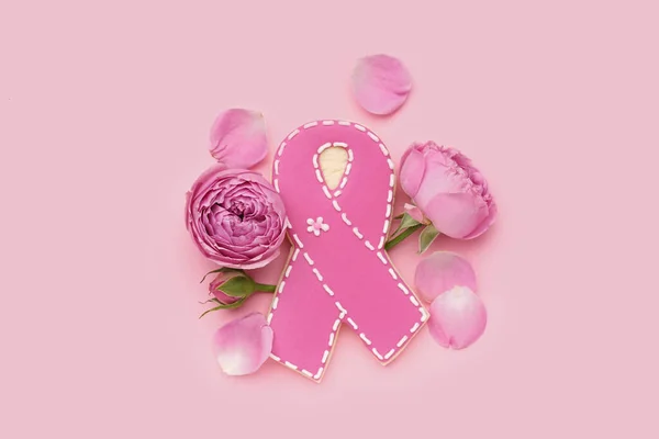 Cookie in shape of ribbon and rose flowers on pink background. Breast cancer awareness concept
