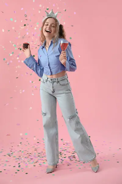 Happy young woman with Birthday muffin and drink on pink background