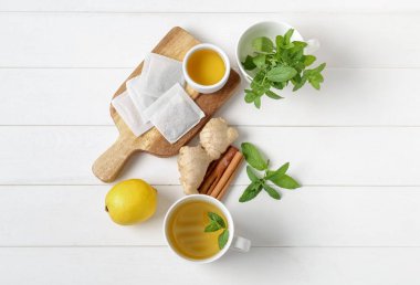 Beyaz ahşap masada zencefil kökü, limon, bal ve tarçınlı taze nane çayı.