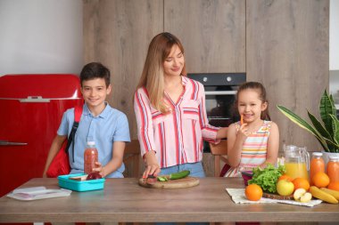 Anne, küçük çocuklarına mutfakta öğle yemeği hazırlıyor.