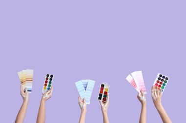 Renk örnekleri ve eflatun arkaplanda suluboya boyalar olan kadın elleri