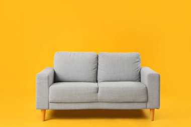 Sarı arka plandaki rahat gri kanepe