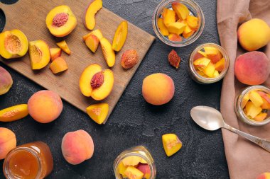 Tatlı şeftali reçelli kavanozlar ve siyah arka planda taze meyveler.