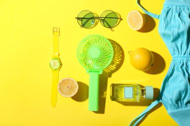 Taşınabilir elektrikli vantilatör, taze limonlar ve sarı arka planda şık kadın aksesuarları.