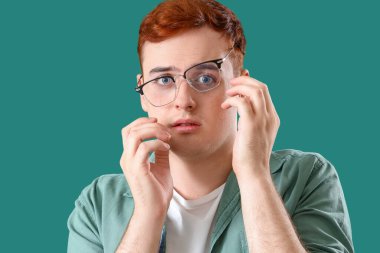 Yeşil arka planda gözlüklü ürkek genç adam, yakın plan.