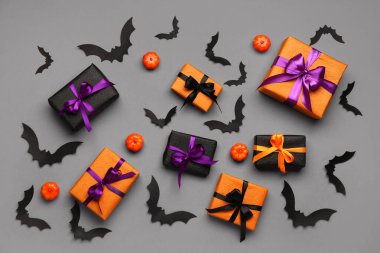 Cadılar Bayramı partisi için balkabaklı kağıt yarasalar ve gri arka planda hediye kutuları.