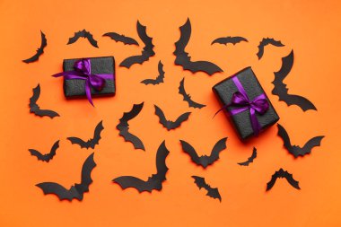 Cadılar Bayramı partisi için kağıt yarasalar ve turuncu arka planda hediye kutuları.