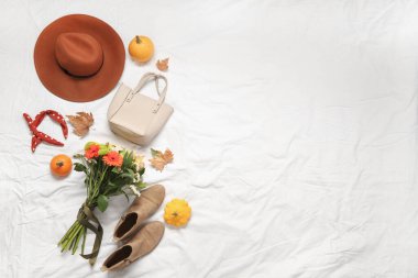 Güzel sonbahar kompozisyonu şık kıyafetler, yapraklar, balkabakları ve beyaz çarşaf üzerinde çiçek demeti