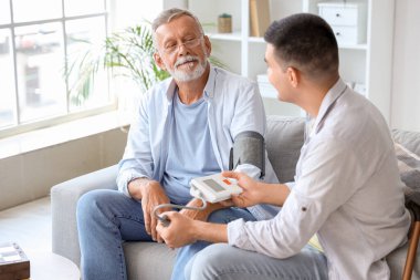 Evde babasının tansiyonunu ölçen genç bir adam var.